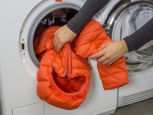 Eine VAUDE Daunenjacke wird in eine Waschmaschine gesteckt.